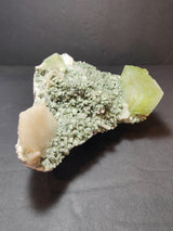 Green apophyllite cubic crystals and peach stilbite clusters atop a textured pale green heulandite matrix against a dark background.