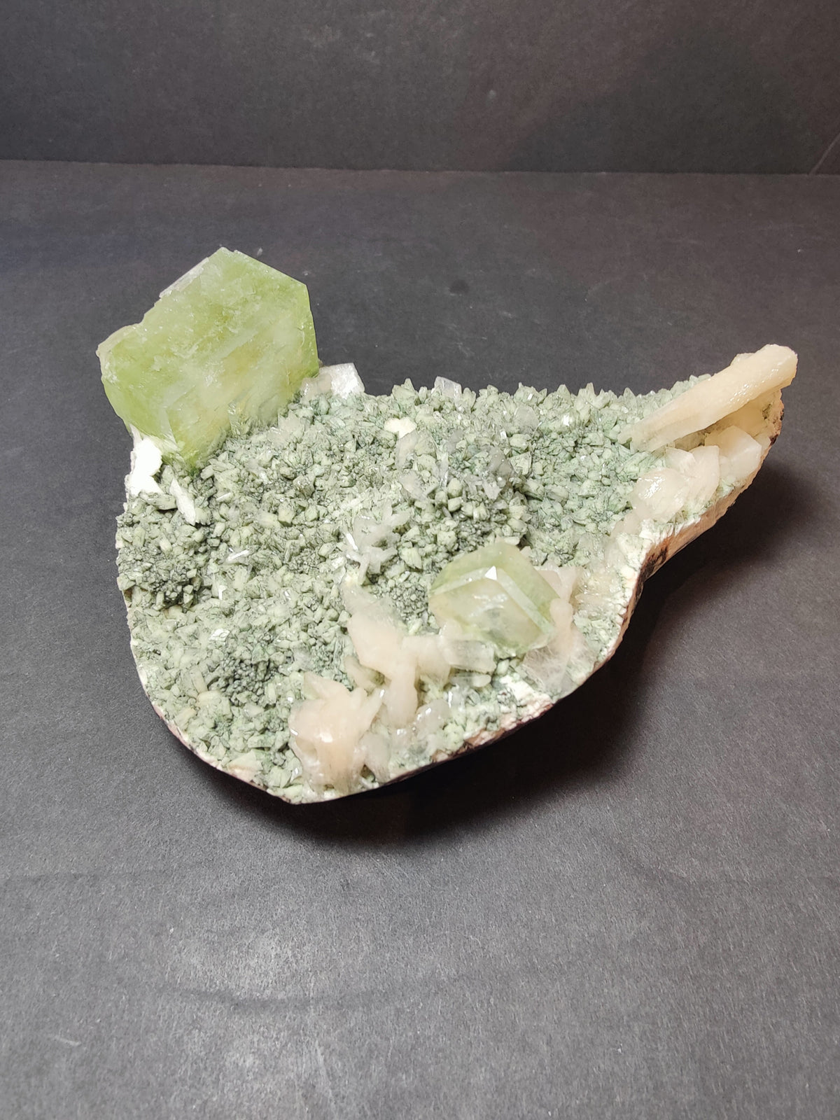Green apophyllite cubes and peach stilbite crystals on a pale green heulandite matrix, displayed on a dark surface.
