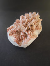 Cluster of elongated, spiky red and white Mordenite crystals with Stilbite on a dark background, showing intricate, layered formations.
