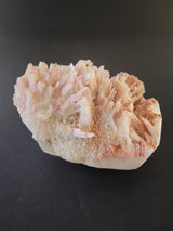 Cluster of pale pink and white crystal formations with fine, elongated, radiating structures on a dark background.