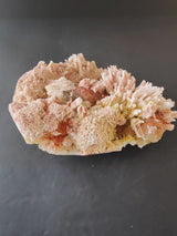 Cluster of pale pink and white Mordenite crystals with elongated Stilbite formations on a gray background, showing textured and spiky mineral growths.