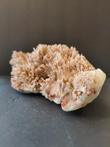 Cluster of pale pinkish-beige stilbite crystals growing densely on a rough white and reddish matrix against a dark background.