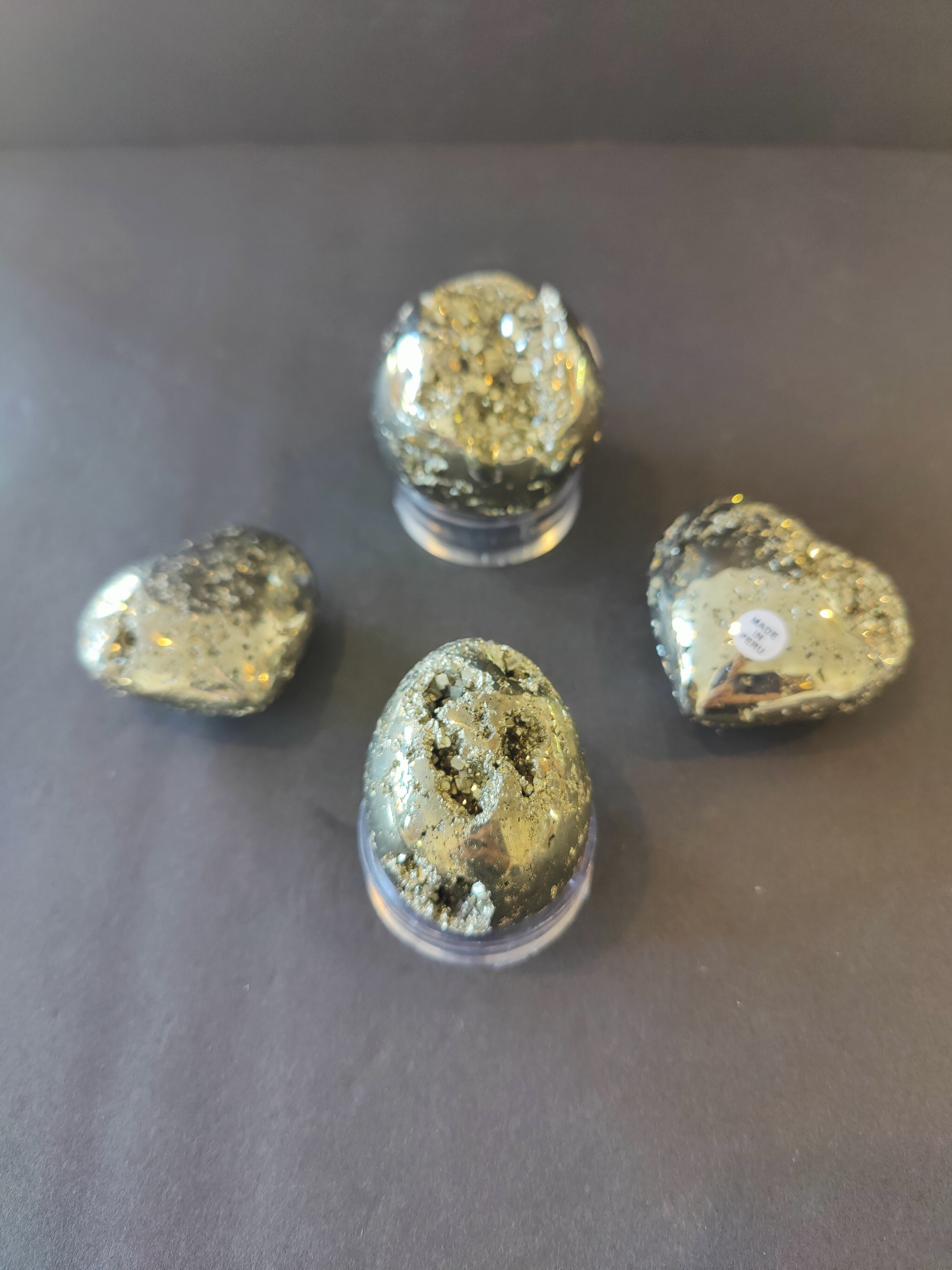 Polished pyrite spheres, eggs, and heart-shaped figurines on a dark textured surface