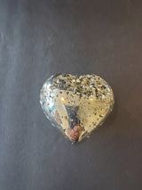 Heart-shaped polished pyrite with reflective metallic surface and scattered flecks of pyrite crystals on top, shown against a dark background.