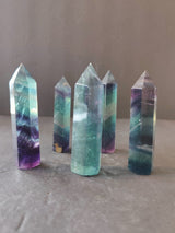 Five polished fluorite towers standing upright, showing bands of green, purple, and clear colors with pointed tops on a neutral surface and background.