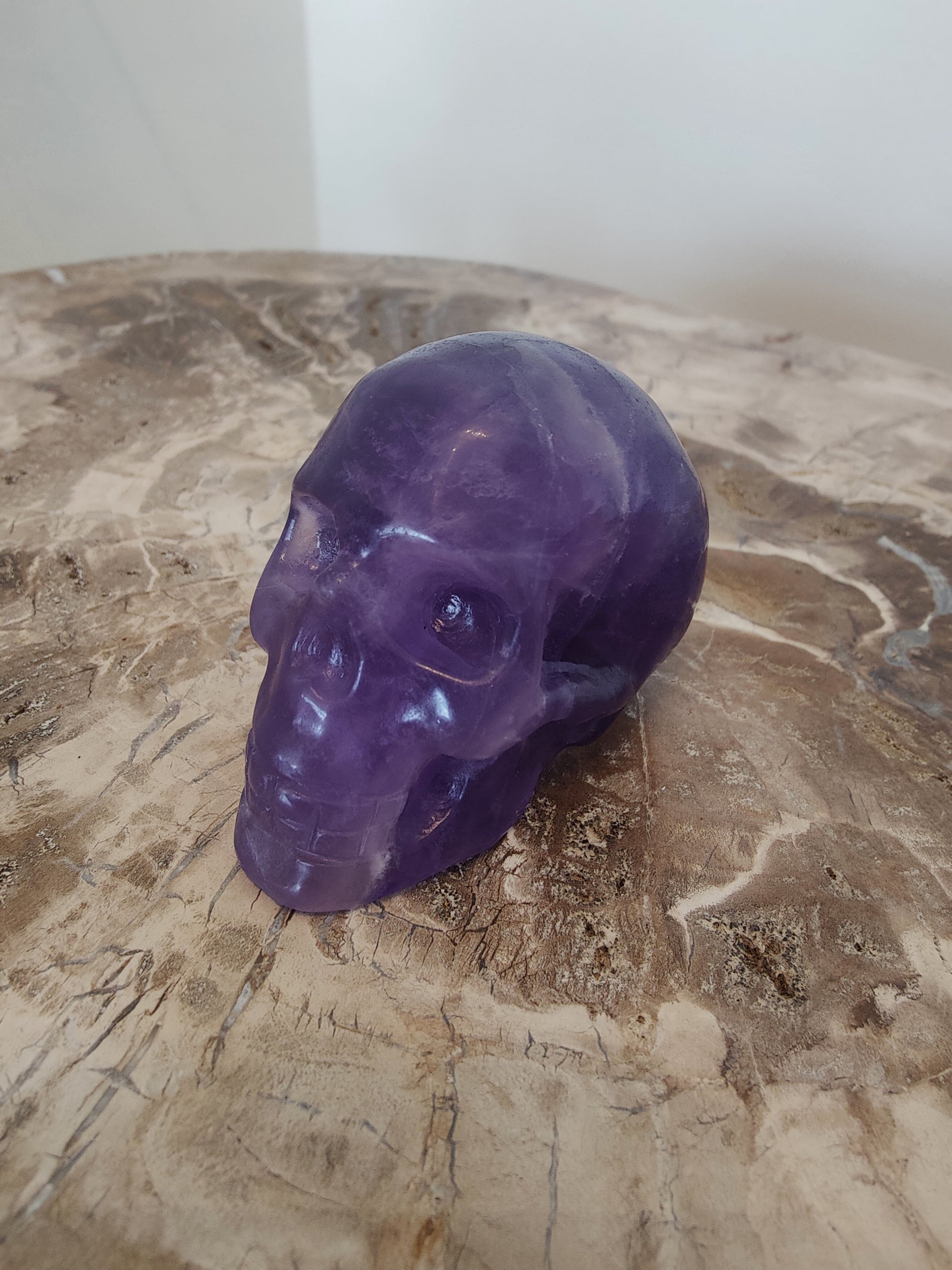 Purple Fluorite Skull Sculpture resting on a pale surface showing smooth polished surfaces and natural purple color variations.