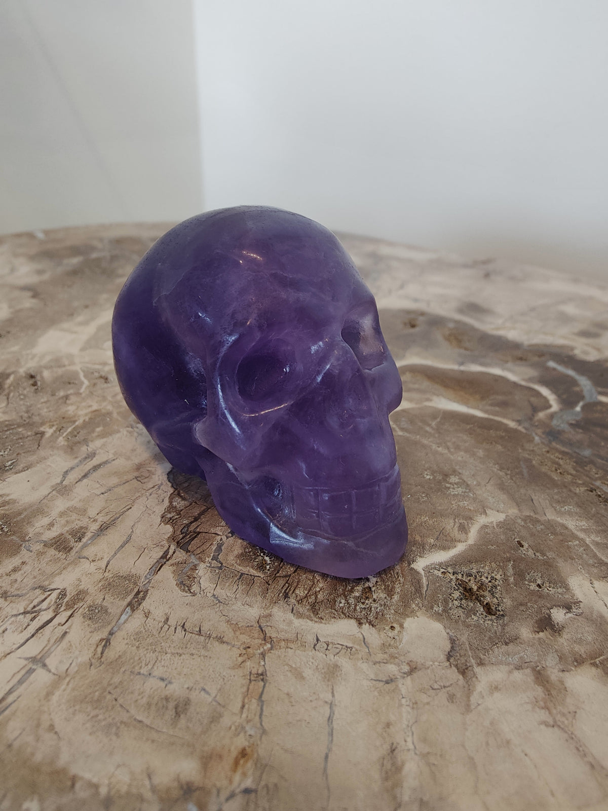 Smooth purple fluorite skull sculpture resting on a textured natural wood surface with visible grain patterns
