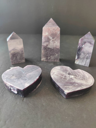 Lepidolite heart and tower sculptures with soft purple hues, displayed on a white surface with diffused light.