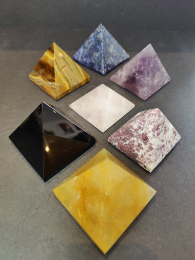 Crystal polished pyramid sculpture from assortment of stones, displayed on a white surface.