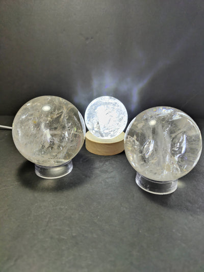 Clear Quartz polished spherical sculpture on a black stand with a light blue gradient background