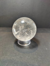 Polished clear quartz sphere with natural inclusions resting on a transparent round stand against a dark background.