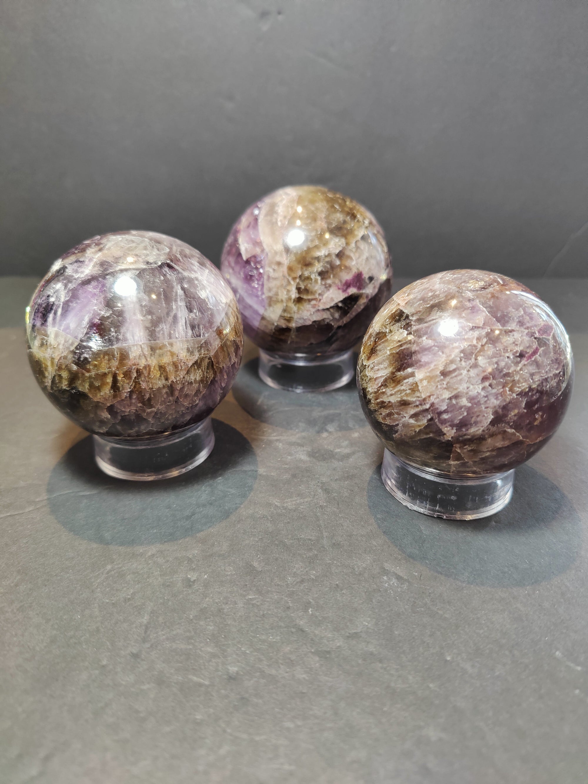 Polished Cacoxenite Amethyst sphere sculpture showing deep purple and golden mineral inclusions
