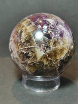 Polished spherical sculpture displaying purple amethyst and earthy brown cacoxenite mineral patterns on a transparent stand against a gray background.