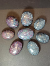 Eight polished oval palmstones displayed on a dark surface, featuring mixed colors of deep blue, purple, and speckles of red and white