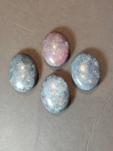 Four polished oval stones on gray background, three with blue tones and one with pinkish-red hues, showing smooth surfaces and natural mineral patterns.