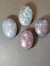 Four polished ruby kyanite stones with deep purple, blue, and teal hues arranged on a dark gray surface, showing smooth oval and rounded shapes.
