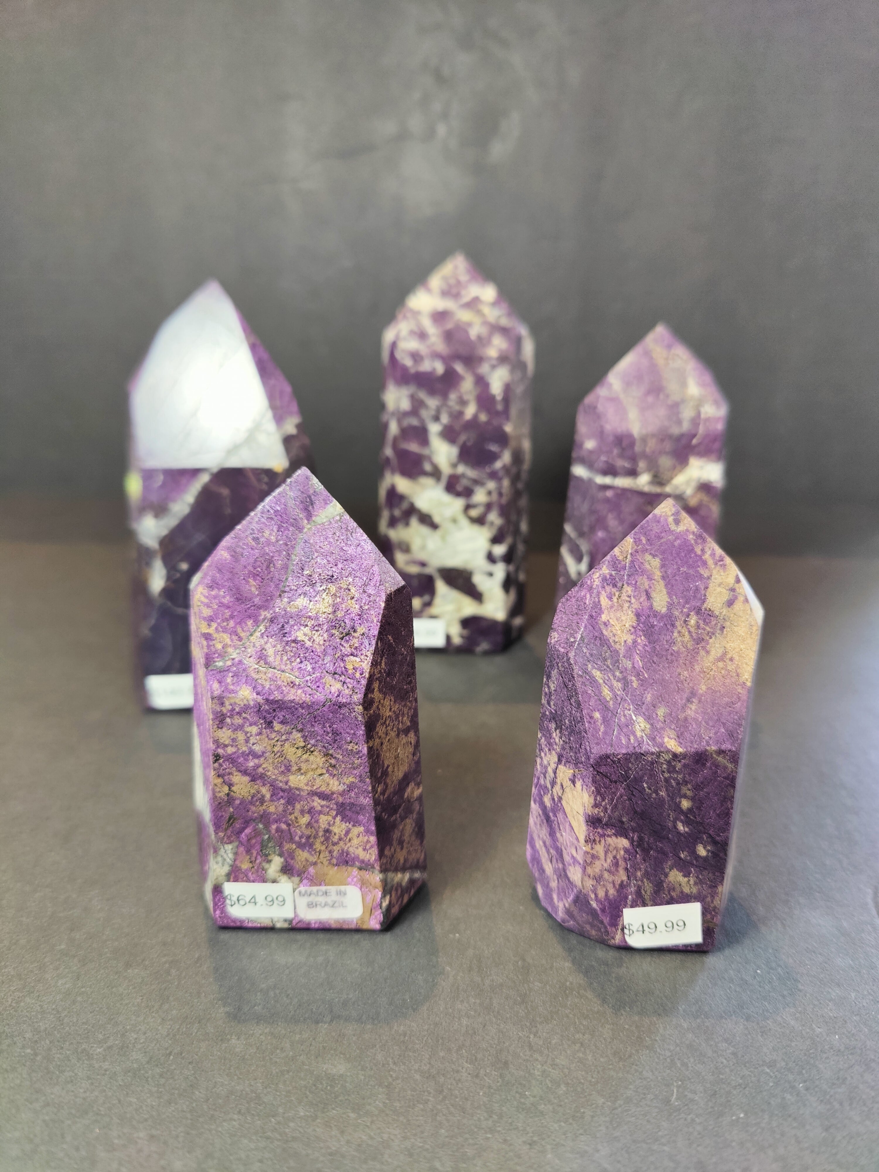 Polished Purpurite obelisk tower sculptures in various sizes displayed on a wooden surface
