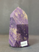 Polished purpurite obelisk tower sculpture with purple and beige mottled patterns, standing upright on a gray surface with a $49.99 price sticker