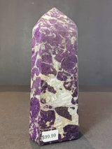 Polished obelisk-shaped purpurite stone with irregular purple and white marbled patterns standing upright against a gray background, labeled with a $99.99 price tag.