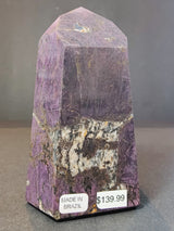 Purpurite polished obelisk tower sculpture with a mix of deep purple and white patterns, displayed on a black surface with price and origin stickers.
