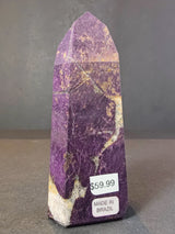 Polished purpurite obelisk-shaped tower with purple and cream marbled patterns, labeled with price and origin on a gray surface.