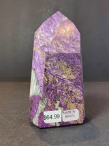 Polished purpurite obelisk tower with vibrant purple and beige mineral patterns, standing upright on a dark surface with price and origin labels.