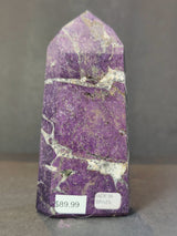 Polished purple Purpurite obelisk tower with white and gray matrix veins, standing upright on a gray surface with price and origin labels visible.