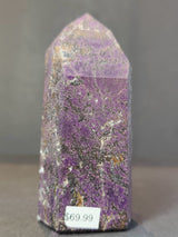 Polished purpurite obelisk tower sculpture with purple hues, black veining, and patches of white and brown, standing upright with a pointed top and price tag of $69.99.