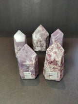 Various sizes of lepidolite polished obelisk tower sculptures, showing purple and white mineral patterns