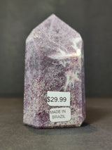 Polished lepidolite obelisk sculpture with purple and white crystal patterns, standing upright with price and origin stickers on front base.