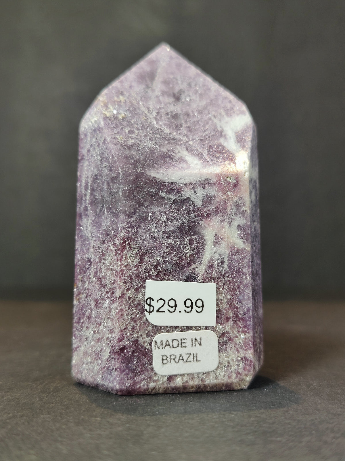 Polished lepidolite obelisk sculpture with purple and white crystal patterns, standing upright with price and origin stickers on front base.