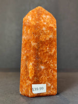 Polished sunstone obelisk tower sculpture with deep orange and white speckled pattern, standing upright with a price tag of $39.99 on front base.