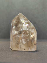 Clear quartz point with internal crackle fractures creating rainbow reflections, standing upright against a plain gray background.