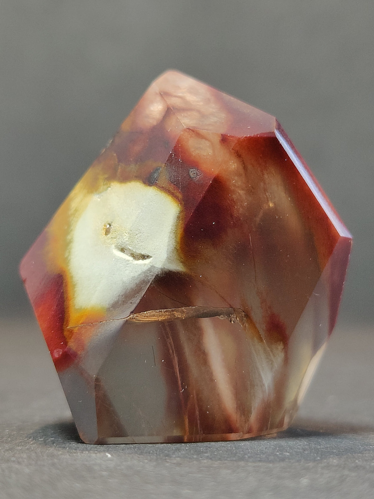 Polished freeform quartz with reddish-brown, cream, and translucent white hues, featuring smooth faceted surfaces and an irregular pentagonal shape on gray background.