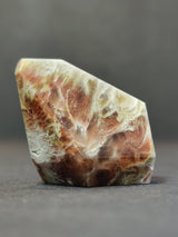 Polished quartz freeform with translucent creamy white and reddish-brown patterns resembling wispy clouds and earthy swirls against a gray gradient background.