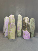 Five polished Atlantisite towers with a pointed hexagonal shape, featuring green and purple hues with natural veining, standing upright on a dark surface.