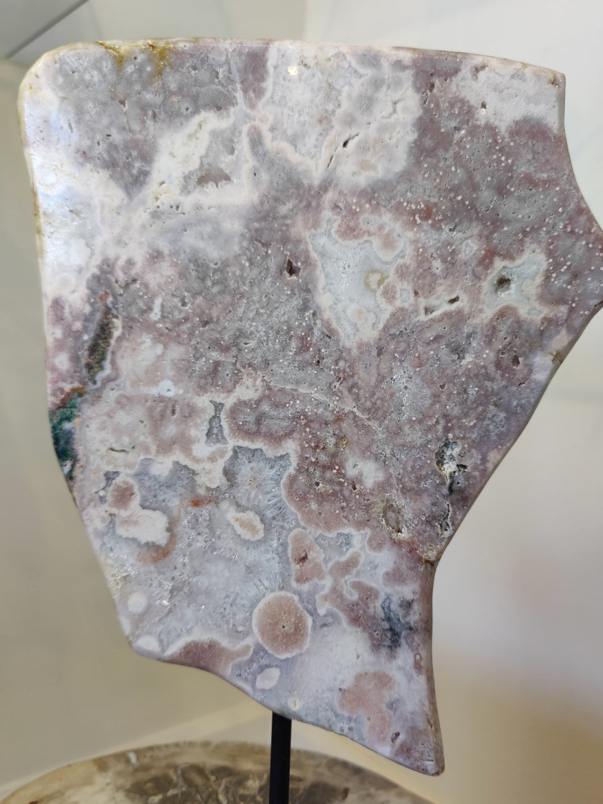 Polished pink amethyst slab with mottled patterns in soft gray, lavender, and white, mounted on a black metal display stand.