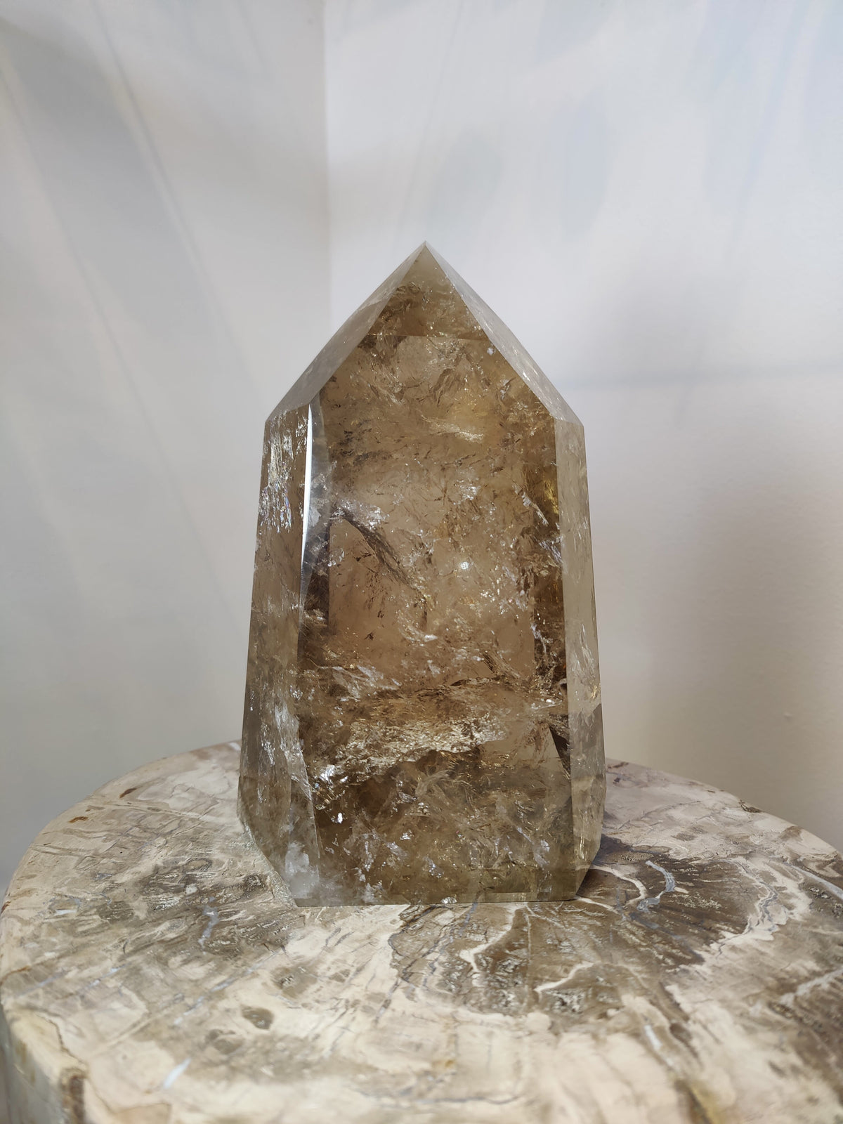 Polished natural citrine crystal point with translucent amber and smoky brown hues, standing upright on a light-colored textured stone surface.