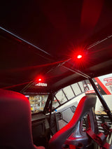 Interior roof of a UTV showing two bright red dome lights mounted on metal roll bars above black bucket seats with visible shelving and signage outside the vehicle.