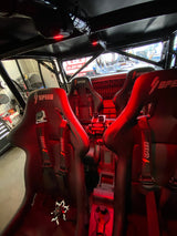 Interior view of a UTV featuring four black bucket seats with red 'SPEED' logos and harnesses, illuminated by a red dome light from above.