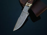 Fixed blade hunting knife with patterned Damascus steel blade and walnut and stag horn handle, resting on a brown leather sheath against a dark background.