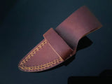 Brown leather sheath with decorative yellow stitching and a wide belt loop, shown against a dark background from an angled top view