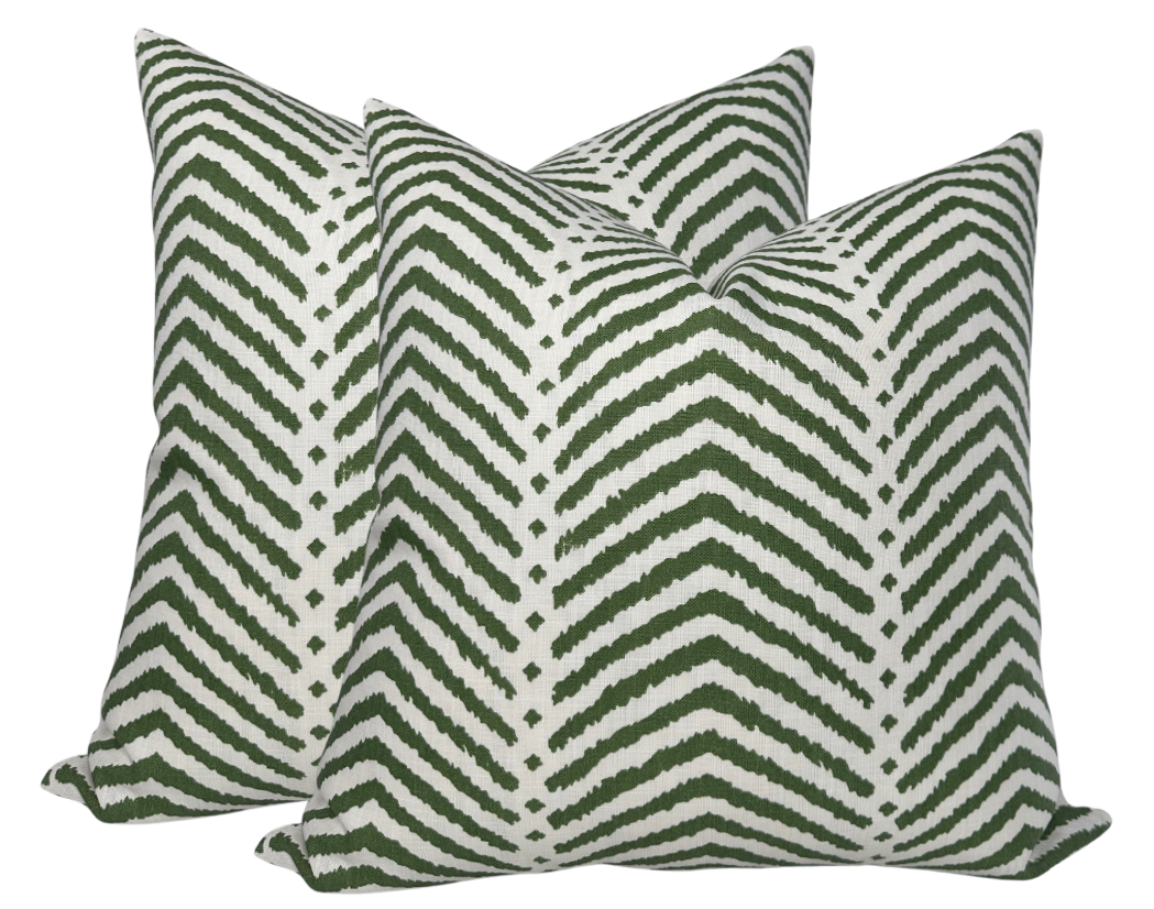 Pair of square pillow covers with a white background and a green zigzag chevron pattern, shown upright and slightly overlapping.