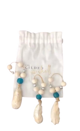 Three oyster-shaped ornaments attached to beaded loops with teal and natural wooden beads, displayed on a white drawstring bag with gold lettering.