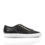 Side view of a black leather sneaker with a smooth toe cap, gold eyelets, black laces, and a thick white rubber sole.
