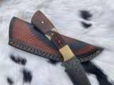 Handmade Damascus steel hunting knife with etched blade, black walnut and stag horn handle scales, brass bolster, resting on a textured brown leather sheath on fur background.