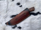 Hunting knife sheathed in brown leather with black burnished edges and tan stitching, wooden handle partially visible, resting on white animal fur with black spots.