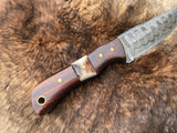 Damascus steel skinning knife with patterned blade, rosewood handle with brass pins, and stag accent, resting on a fur background.
