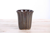 Dark honey-colored ceramic bonsai pot with vertical ridges and a scalloped rim, shown on a light wooden surface against a white background.