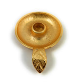 Round golden candlestick holder dish with a textured surface and a leaf-shaped handle extending from its base, shown from above on a white background.